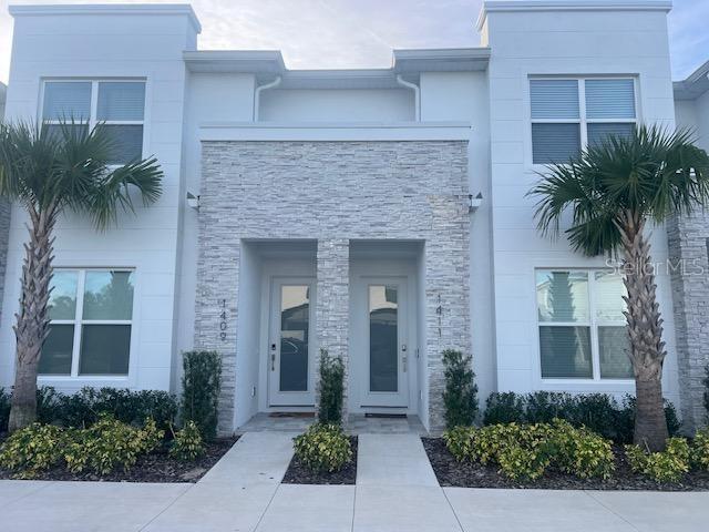 A modern two-story duplex with white stucco walls, stone veneer accents, and two palm trees — 1411 SERENDIPITY LANE, CLERMONT, FL