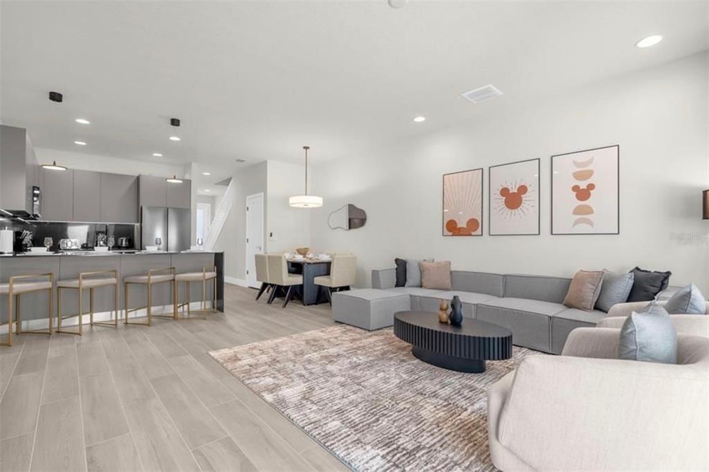 An open-concept living and dining area features gray cabinetry, light wood flooring, and modern furniture — 1411 SERENDIPITY LANE, CLERMONT, FL