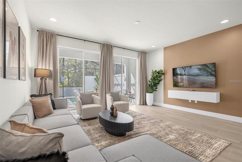 A modern living room features a tan accent wall, a floating console, and sliding glass doors — 1411 SERENDIPITY LANE, CLERMONT, FL