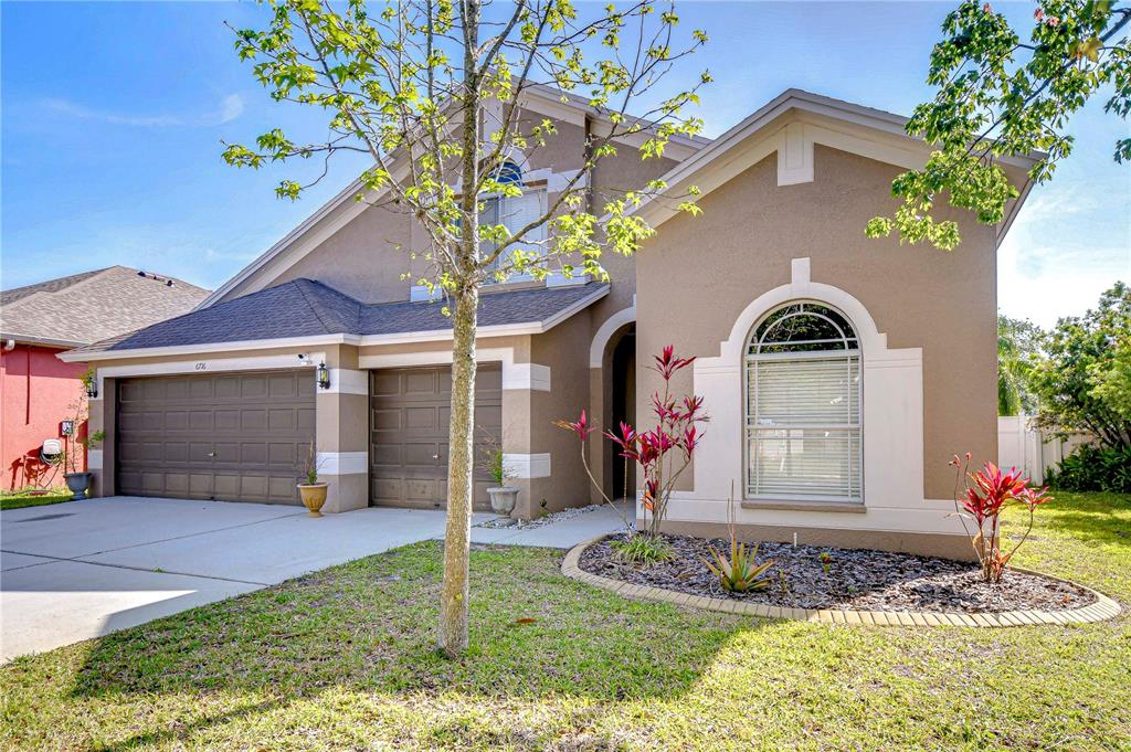 A tan, two-car garage home with a front garden and a large arched window — 6716 BLUFF MEADOW COURT, WESLEY CHAPEL, FL