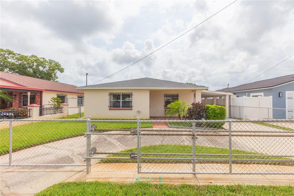 A single-story house with a beige exterior, barred windows, and a chain-link fence in front — 6611 N CLARK AVENUE, TAMPA, FL