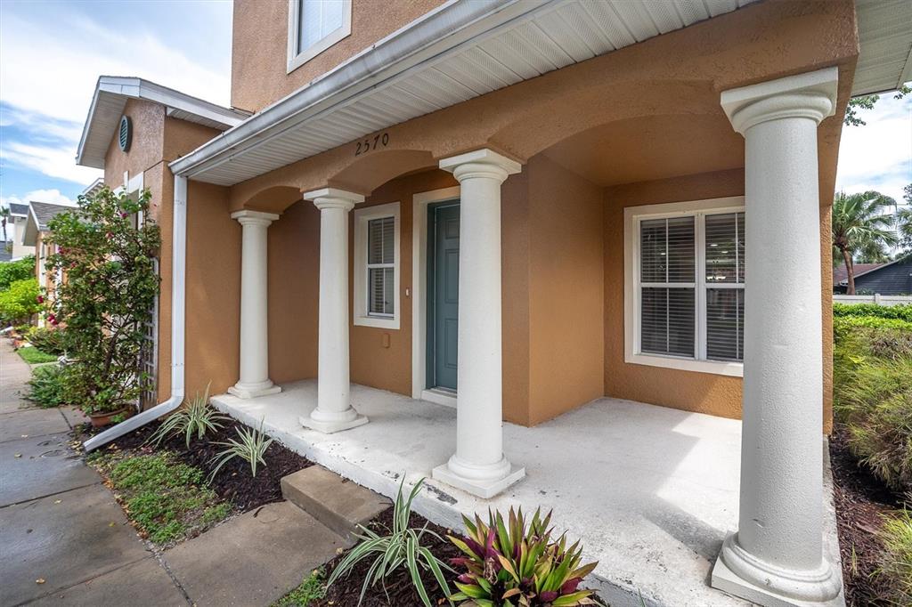 A tan house exterior features a covered porch with white columns and a front door — 2570 SEA WIND WAY, CLEARWATER, FL