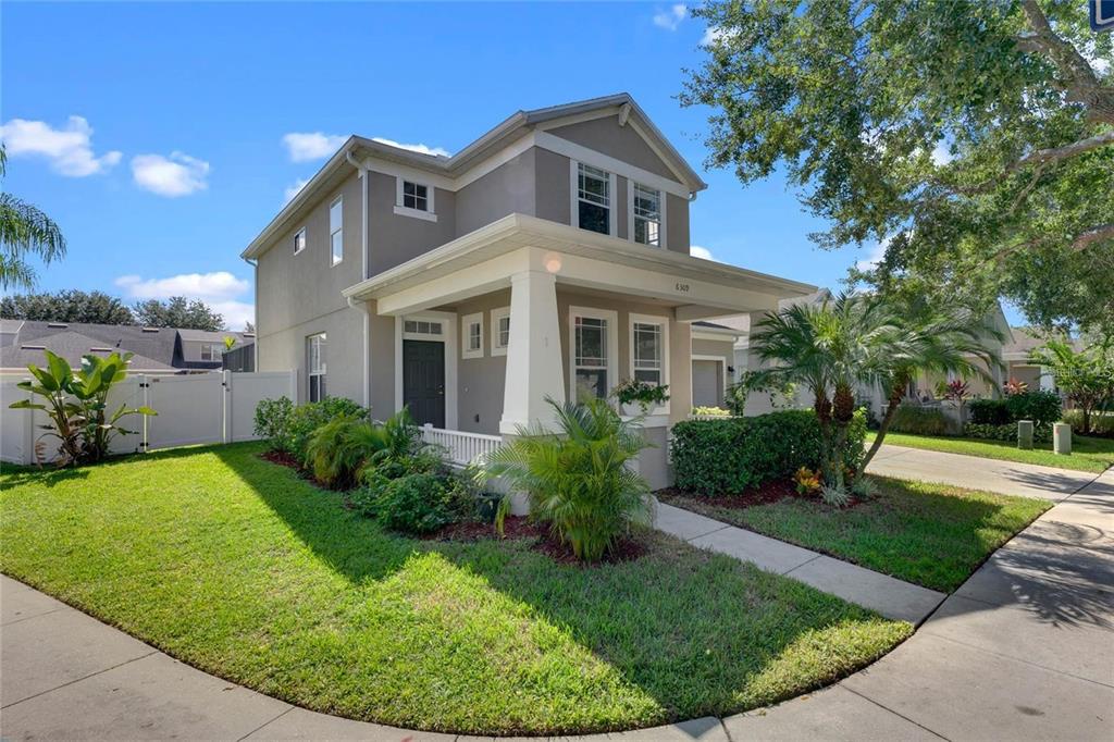 A two-story house with a covered front porch, tan siding, and a white picket fence — 6309 EARTHGOLD DRIVE, WINDERMERE, FL