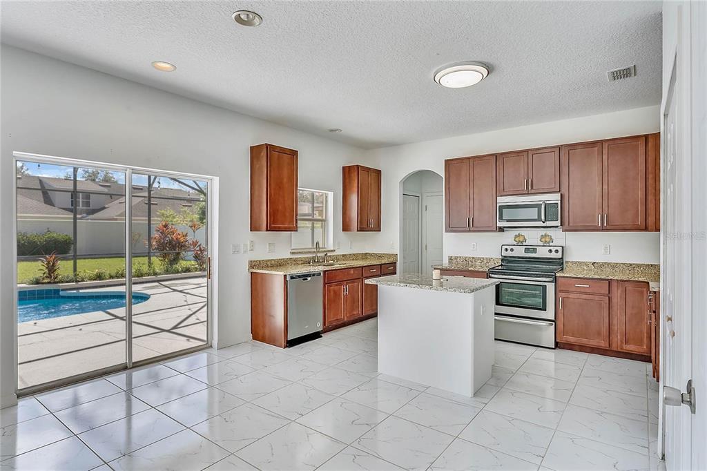 A kitchen with wood cabinets, granite countertops, stainless steel appliances, and a sliding glass door — 6309 EARTHGOLD DRIVE, WINDERMERE, FL