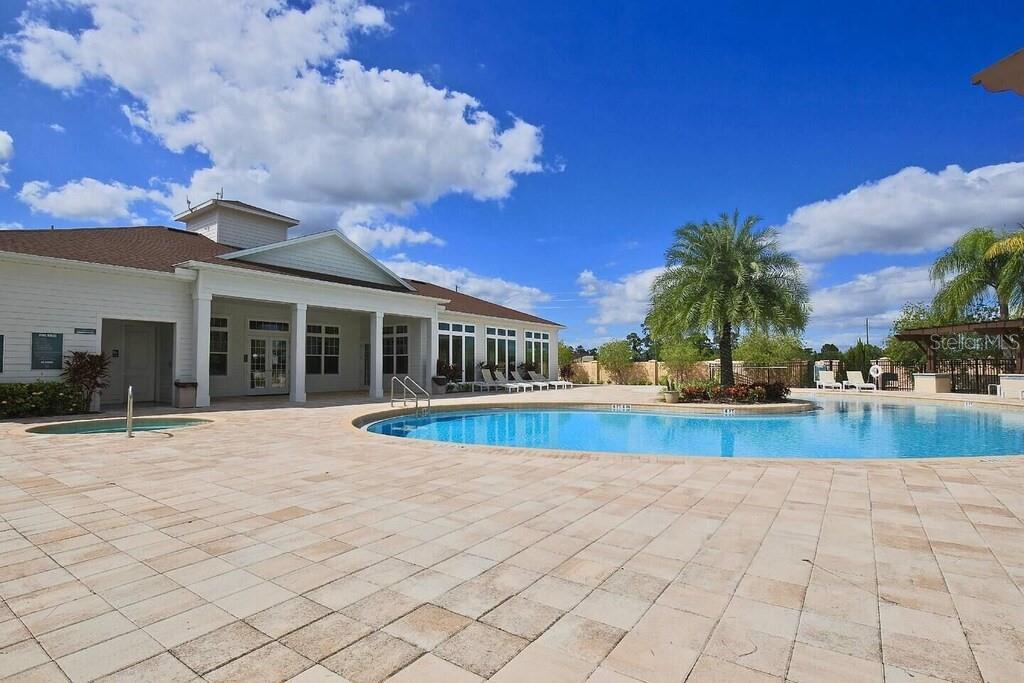 A swimming pool and hot tub sit on a paved patio beside a community clubhouse — 8953 SHINE DRIVE, KISSIMMEE, FL