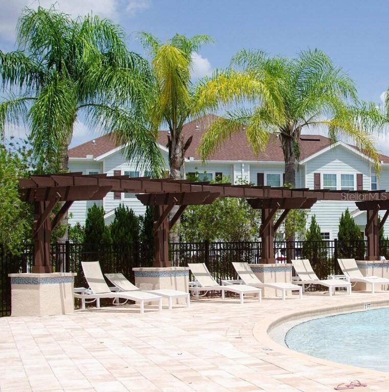A swimming pool area features lounge chairs under a wooden pergola with palm trees nearby — 8953 SHINE DRIVE, KISSIMMEE, FL