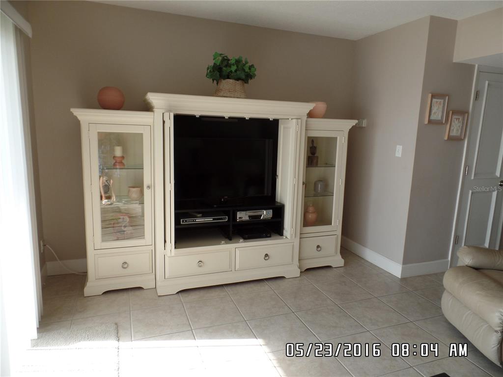 A living room features a large, cream-colored entertainment center with glass-front cabinets on tile flooring — 815 OCEAN SHORE BOULEVARD UNIT 13B, ORMOND BEACH, FL