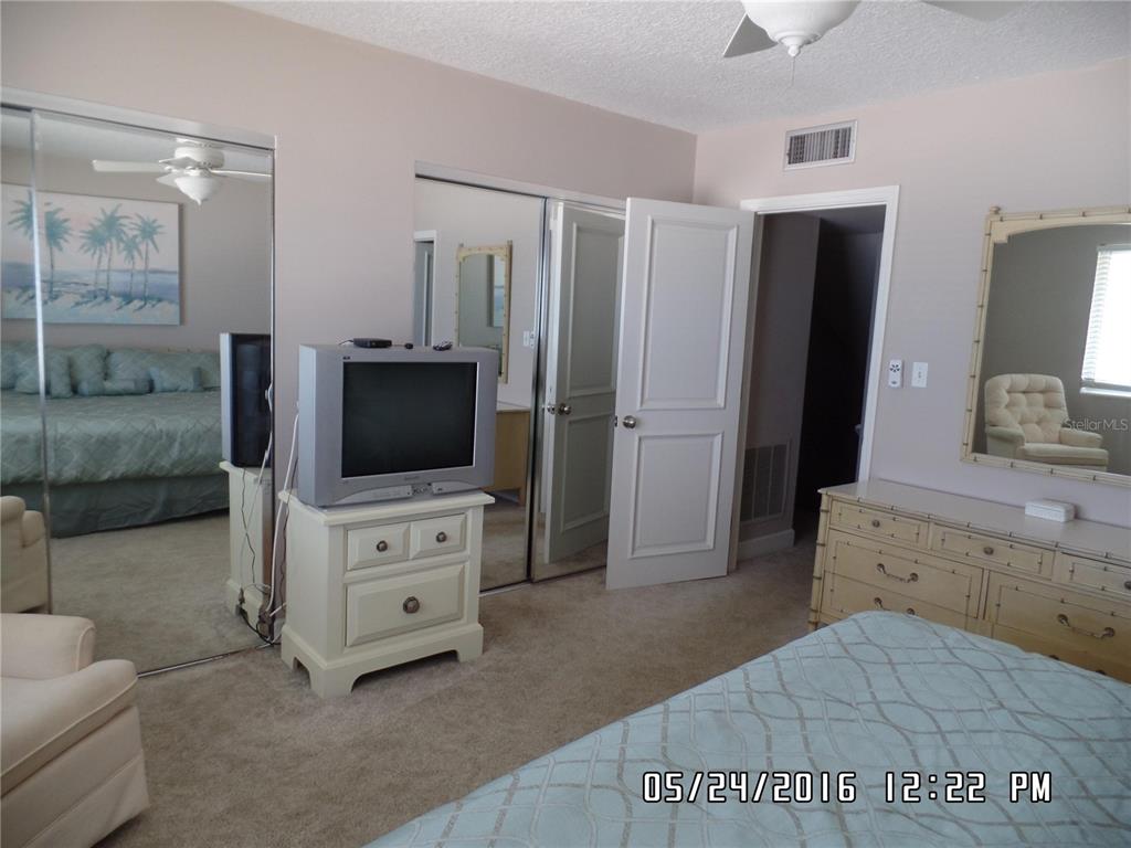 A bedroom features a television on a dresser, mirrored closet doors, and a bed — 815 OCEAN SHORE BOULEVARD UNIT 13B, ORMOND BEACH, FL