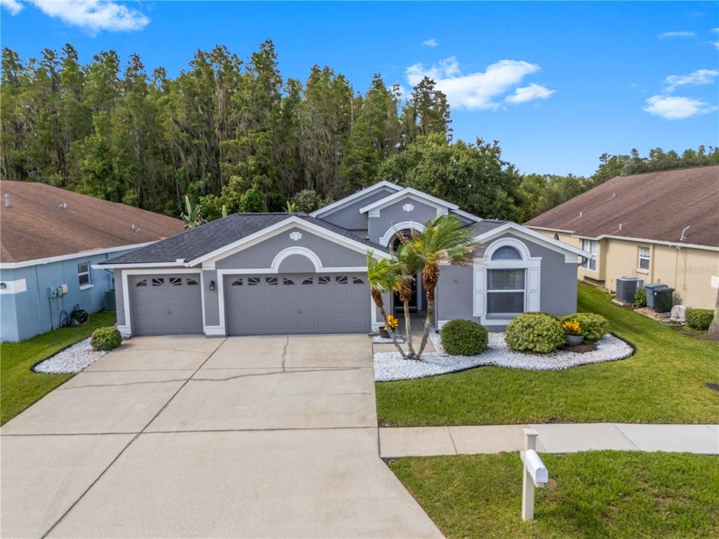 A gray single-story house with a three-car garage and a concrete driveway — 30923 IVERSON DRIVE, WESLEY CHAPEL, FL