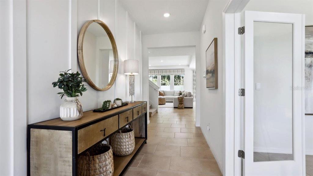 A hallway features a wooden console table, a round mirror, and tile flooring — 2391 STERLING FOREST COURT, WESLEY CHAPEL, FL