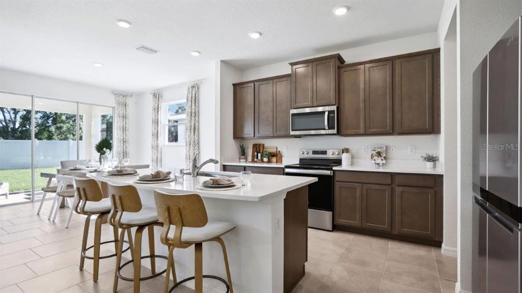 A kitchen with brown cabinets, white countertops, a center island, and stainless steel appliances — 2391 STERLING FOREST COURT, WESLEY CHAPEL, FL