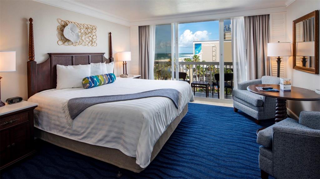 A hotel room features a king bed, blue patterned carpet, and a balcony overlooking the ocean — 5500 GULF BOULEVARD UNIT 5227, ST PETE BEACH, FL
