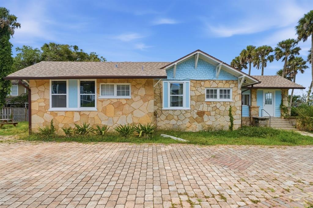 A single-story house with stone siding, blue accents, and a paved driveway under a blue sky — 5202 RIVERSIDE DRIVE, PORT ORANGE, FL