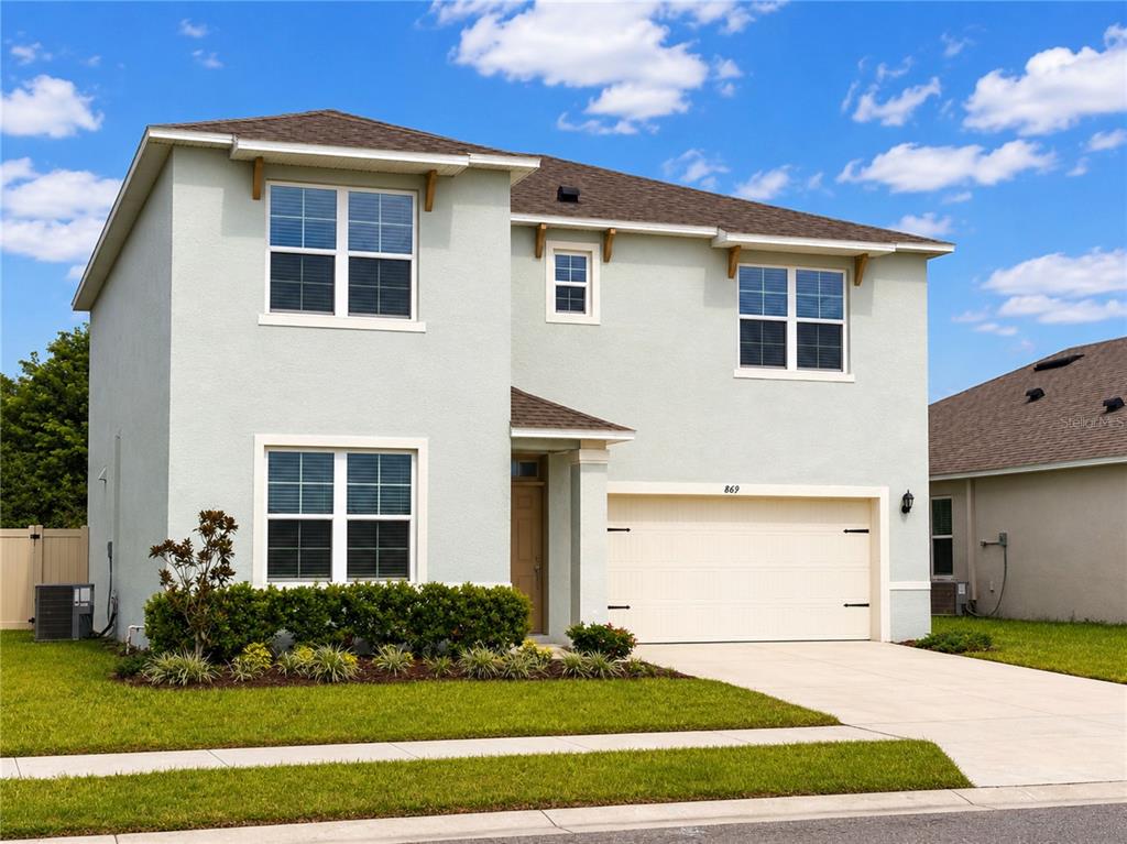 A two-story, light green suburban house features a two-car garage and a front lawn — 869 AMBLESIDE DRIVE, HAINES CITY, FL