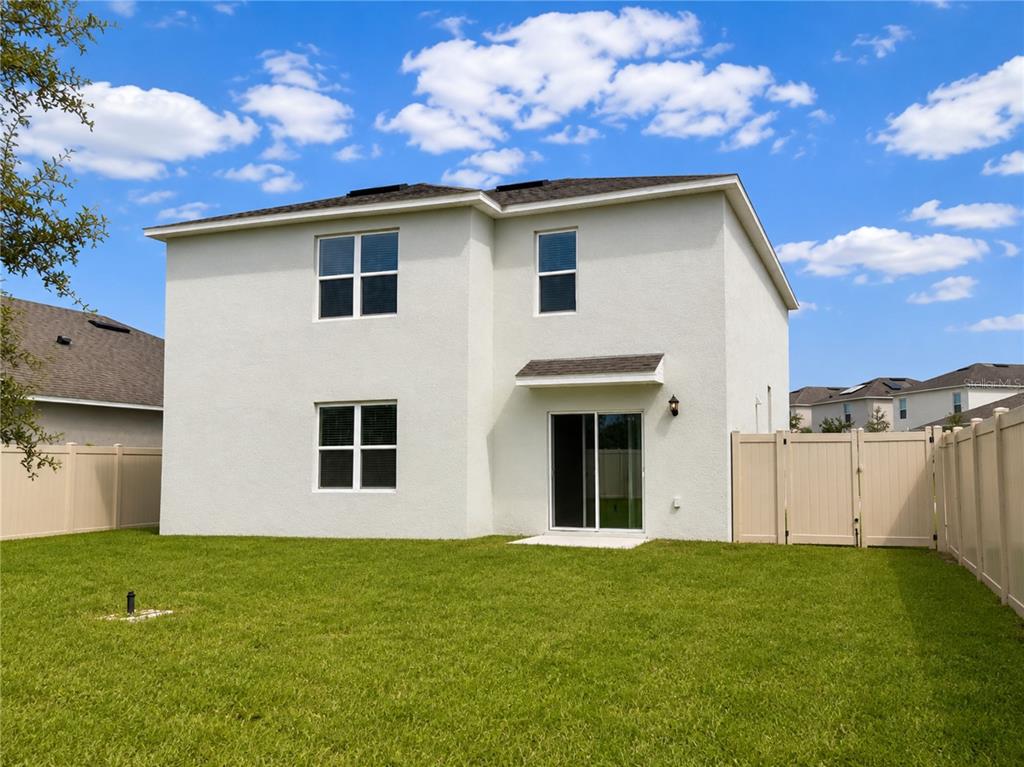The exterior rear view of a two-story house features a grassy yard and vinyl fencing — 869 AMBLESIDE DRIVE, HAINES CITY, FL