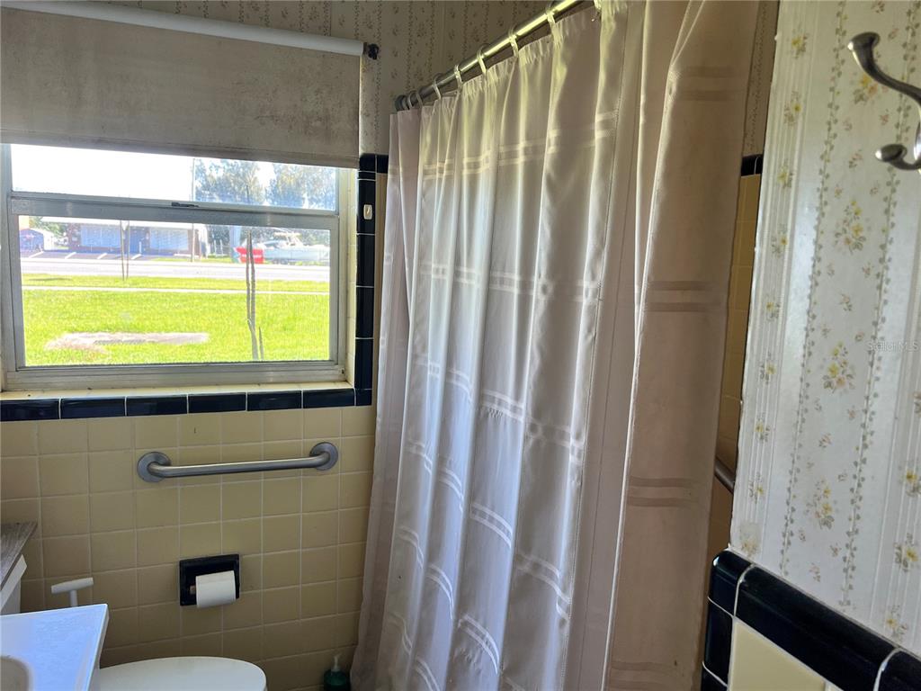A bathroom features yellow tiled walls, a shower with a white curtain, and floral wallpaper — 104 GRACE AVENUE, COCOA, FL