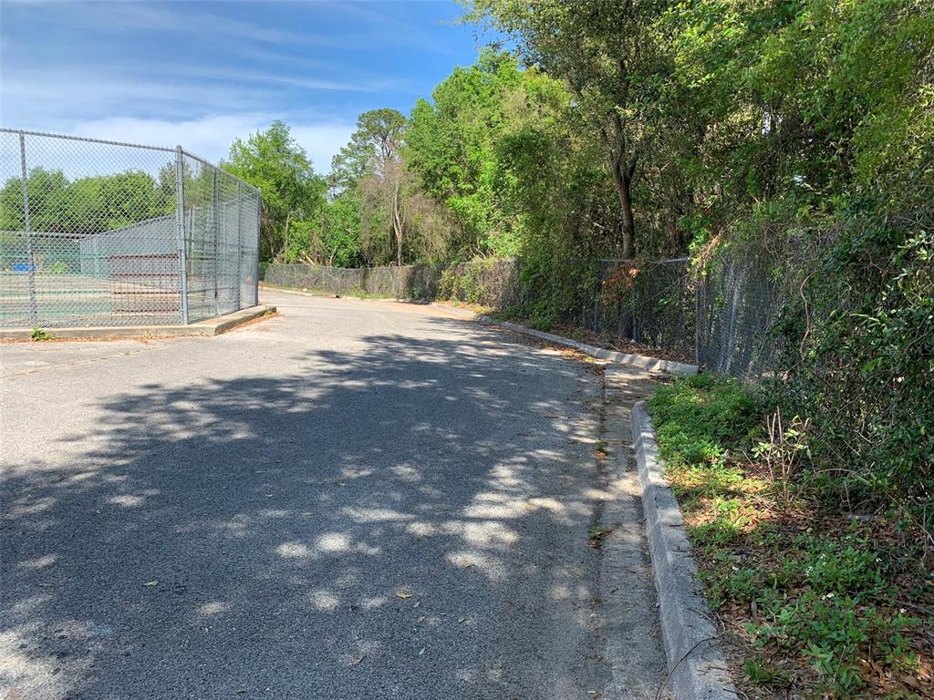 An asphalt path runs alongside a chain-link fence bordering a tennis court and wooded area — NORMANDY BOULEVARD, JACKSONVILLE, FL