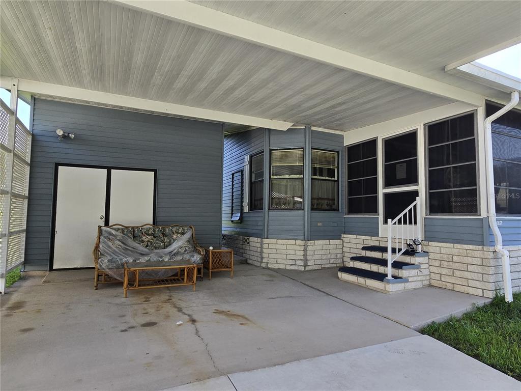 A covered concrete patio features a sofa, a coffee table, and steps leading to a house — 4007 COHEN DRIVE UNIT 742, ZELLWOOD, FL
