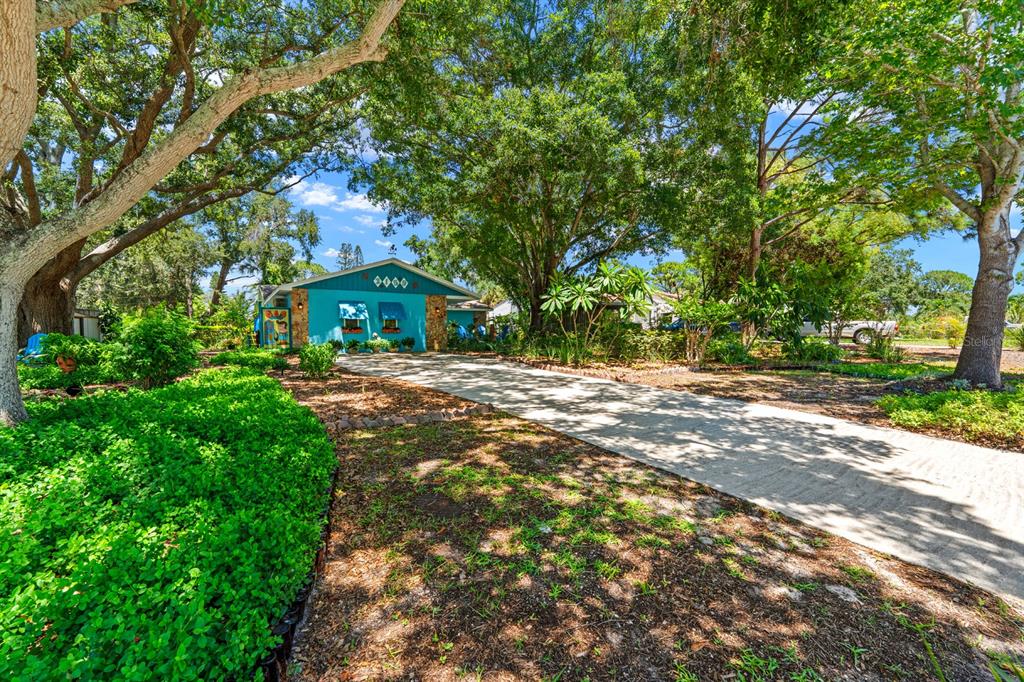 A bright blue house with a long concrete driveway sits under large, leafy oak trees — 2159 BARCELONA WAY S, ST PETERSBURG, FL