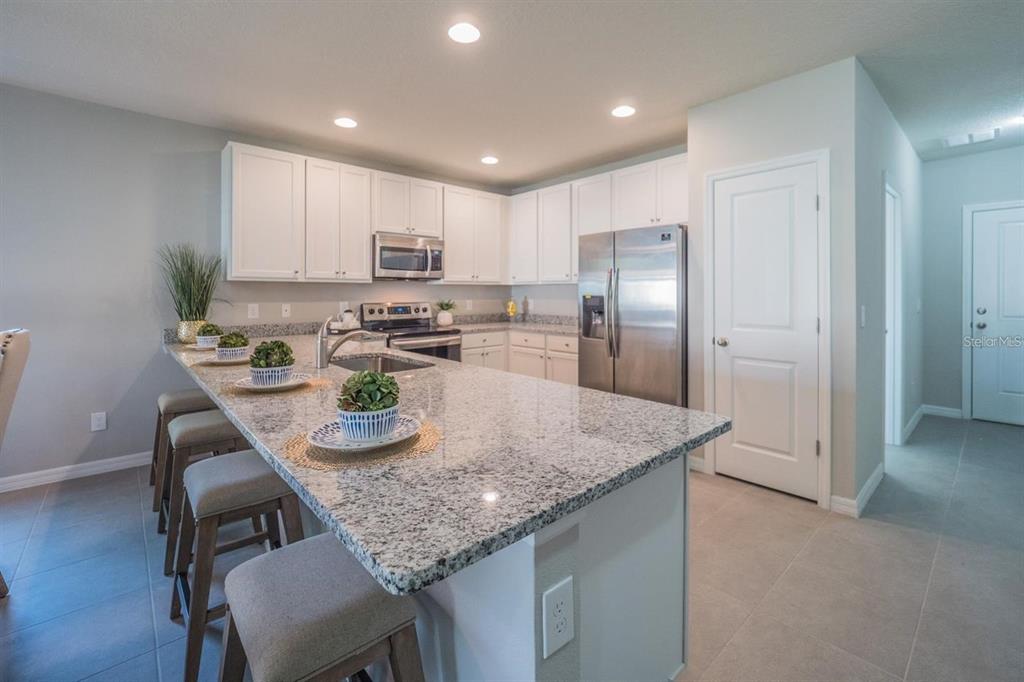 A kitchen with white cabinets, granite countertops, a stainless steel refrigerator, and a breakfast bar — 248 CHESHIRE COURT, KISSIMMEE, FL