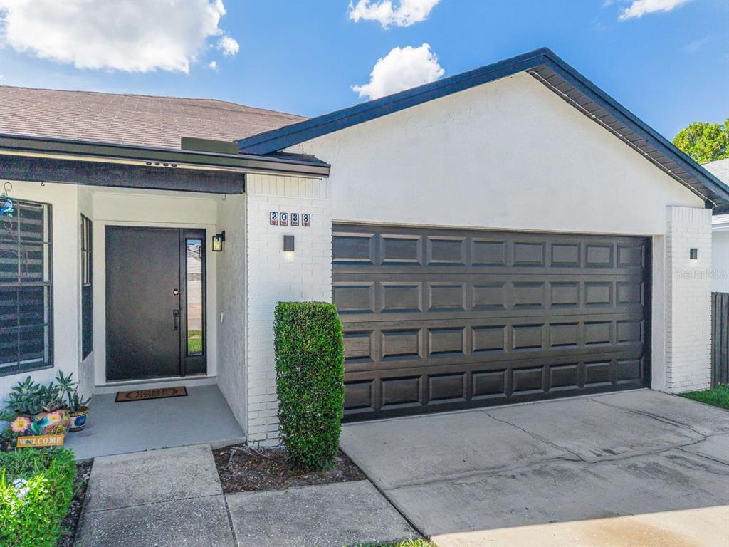 A white brick house exterior features a black garage door and a modern front door — 3038 WOOLRIDGE DRIVE, ORLANDO, FL