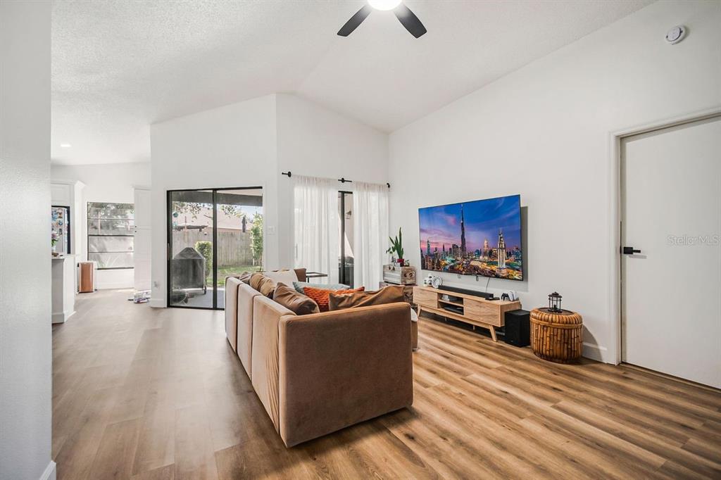 A living room features light wood-look flooring, a tan sofa, and a wall-mounted television — 3038 WOOLRIDGE DRIVE, ORLANDO, FL