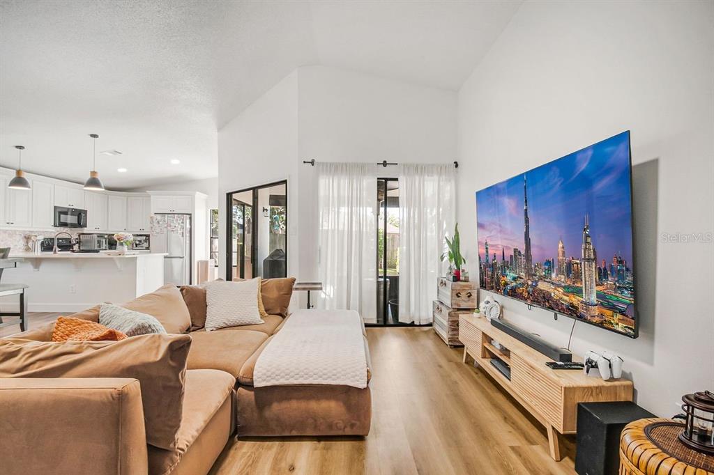 A living room with a large sectional sofa, wood flooring, and a wall-mounted television — 3038 WOOLRIDGE DRIVE, ORLANDO, FL