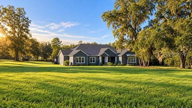 A single-story house with a gray exterior sits in the middle of a large grassy field — 11707 SE 101ST COURT ROAD, BELLEVIEW, FL