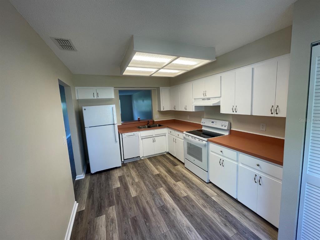 A kitchen features white cabinets, a white refrigerator, a white stove, and wood-look flooring — 6793 E DOWNING STREET, INVERNESS, FL
