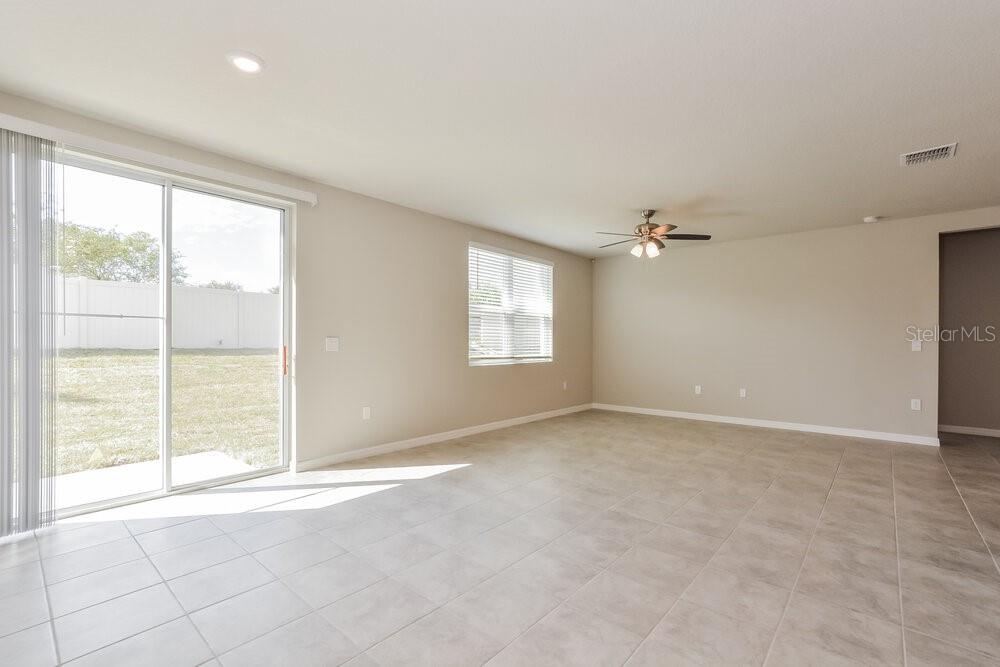 An empty living room features light-colored tile flooring, beige walls, a ceiling fan, and sliding doors — 1026 OAK VALLEY DRIVE, AUBURNDALE, FL