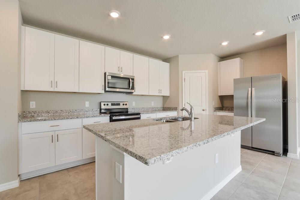 A kitchen features white cabinets, granite countertops, a center island, and stainless steel appliances — 1026 OAK VALLEY DRIVE, AUBURNDALE, FL
