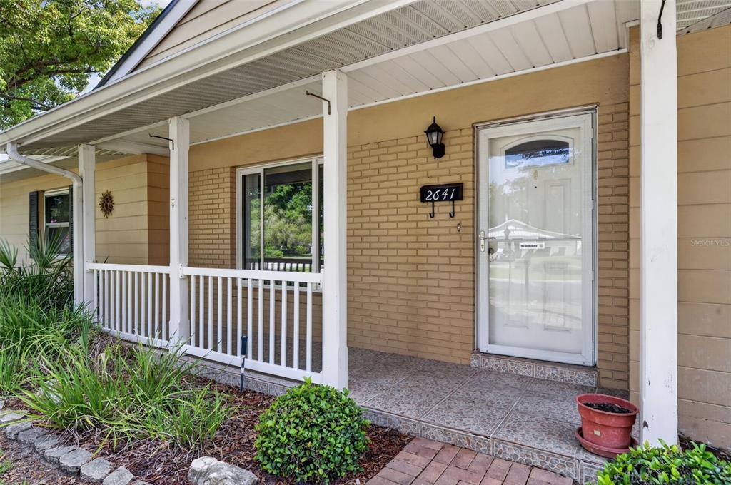 A covered front porch features a brick facade, white railing, and a glass storm door — 2641 CARVELL COURT, WINTER PARK, FL