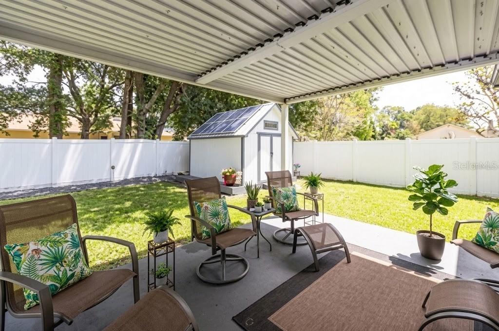 A covered patio overlooks a backyard with a white fence and a shed with solar panels — 6 BOXWOOD LANE, PALM COAST, FL