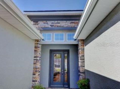 A front entryway featuring a glass-paneled door, stone accents, and a transom window above — 802 ALDENHAM LANE, ORMOND BEACH, FL
