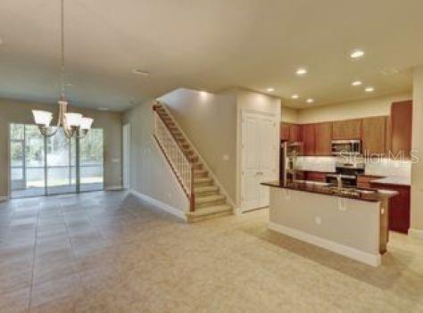 An open-concept kitchen with wood cabinets and a granite island overlooks a staircase and dining area — 802 ALDENHAM LANE, ORMOND BEACH, FL