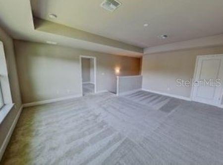 A spacious carpeted room features a tray ceiling, a doorway, and a white interior door — 802 ALDENHAM LANE, ORMOND BEACH, FL