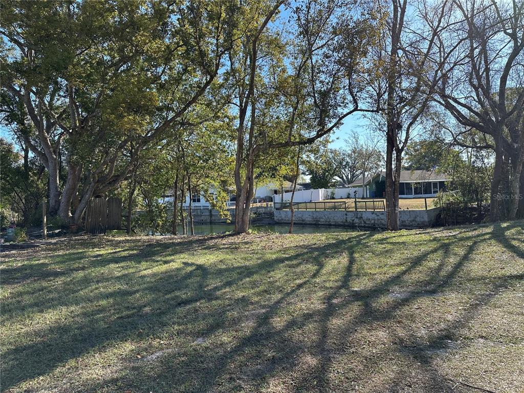 A grassy yard overlooks a canal with a concrete seawall and trees in the background — SUNRISE DRIVE, LUTZ, FL