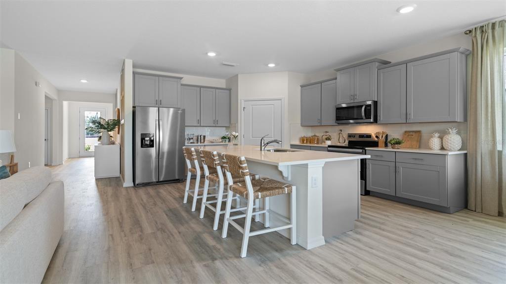 A kitchen features gray cabinets, a white island with bar stools, and light wood flooring — 3033 KINGSMAN TRAIL, ORMOND BEACH, FL