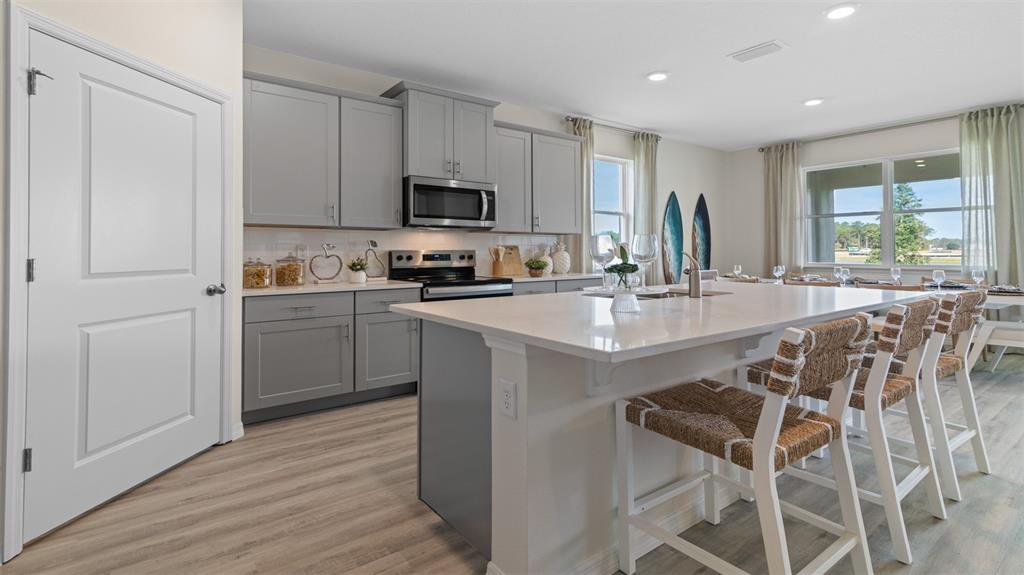 A kitchen features gray cabinets, a large white island with bar stools, and light flooring — 3033 KINGSMAN TRAIL, ORMOND BEACH, FL