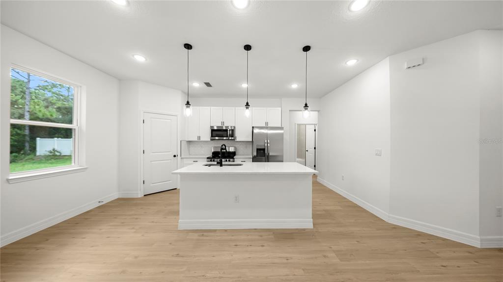 A modern kitchen features white cabinetry, a central island with a sink, and light wood flooring — 9481 N STAFFORD DRIVE, CITRUS SPRINGS, FL