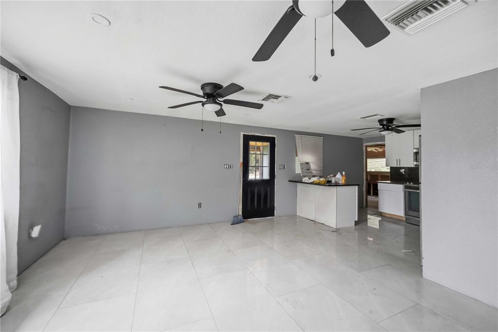A living room with gray walls, white tile flooring, two ceiling fans, and an adjacent kitchen — 4275 SOUTHLAND AVENUE, PORT CHARLOTTE, FL