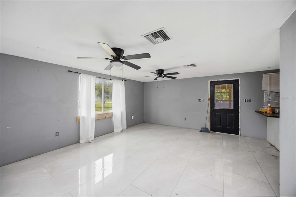 An empty room features gray walls, white tile flooring, two ceiling fans, and a black door — 4275 SOUTHLAND AVENUE, PORT CHARLOTTE, FL