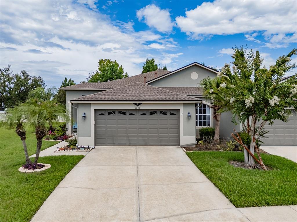 A gray house with a two-car garage and a concrete driveway under a cloudy sky — 1237 AMBRIDGE DRIVE, WESLEY CHAPEL, FL
