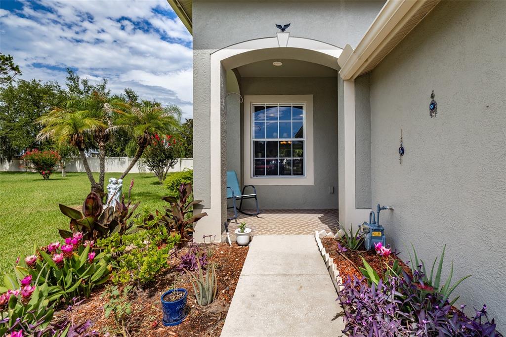 A concrete walkway leads to a covered front porch with a window and a chair — 1237 AMBRIDGE DRIVE, WESLEY CHAPEL, FL
