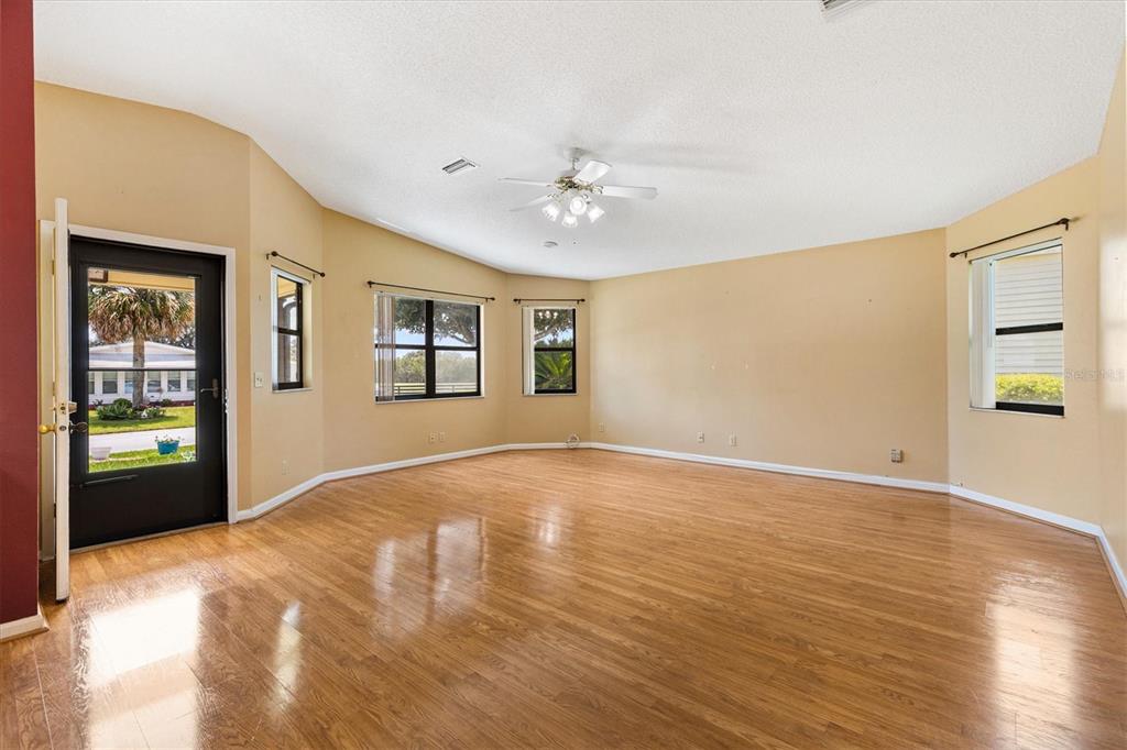 An empty living room features light wood flooring, beige walls, and a ceiling fan — 1532 E SCHWARTZ BOULEVARD, LADY LAKE, FL