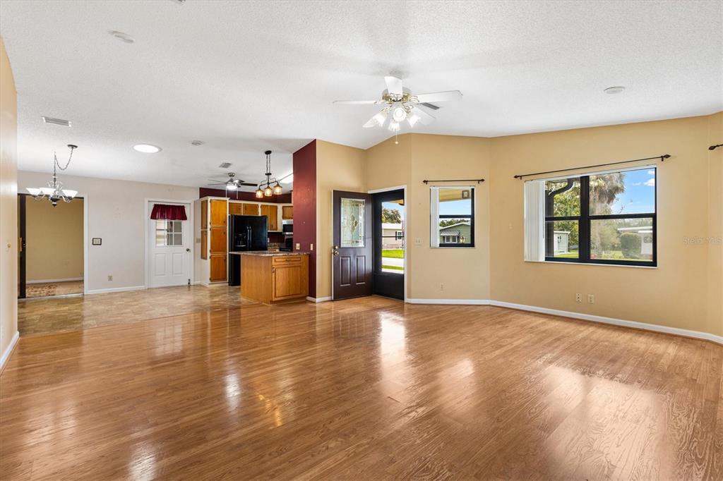 A spacious living room with hardwood floors, a ceiling fan, and an adjacent open kitchen — 1532 E SCHWARTZ BOULEVARD, LADY LAKE, FL