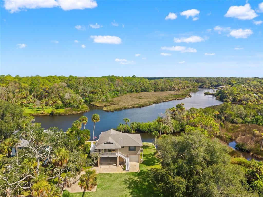 An elevated house sits on a grassy lot beside a winding river and forest — 5350 FELKER DRIVE, WEEKI WACHEE, FL