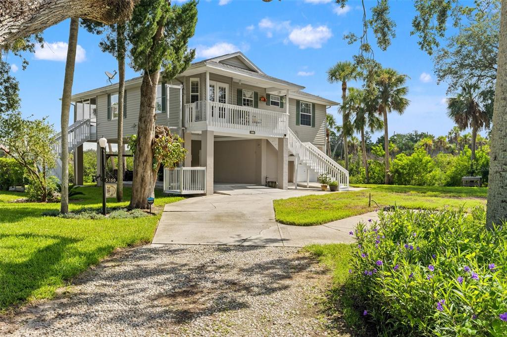 A two-story elevated house with a concrete driveway, white railings, and surrounding trees and greenery — 5350 FELKER DRIVE, WEEKI WACHEE, FL