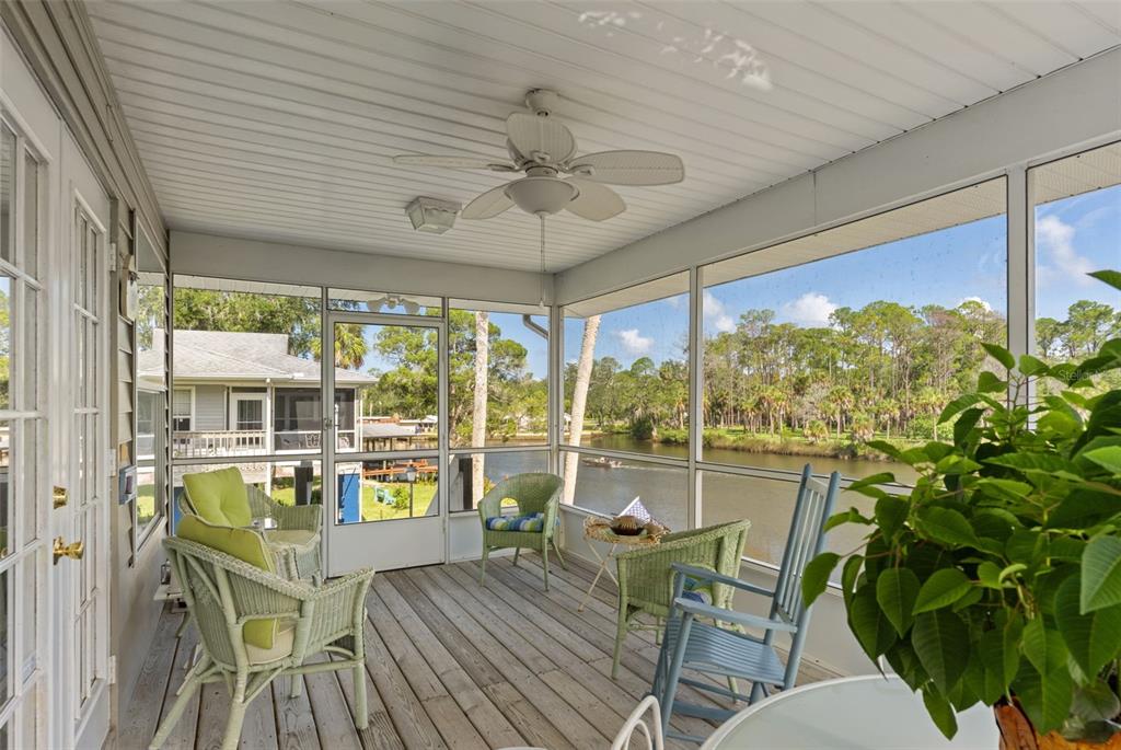 A screened-in porch with wicker furniture and a ceiling fan overlooks a river and trees — 5350 FELKER DRIVE, WEEKI WACHEE, FL