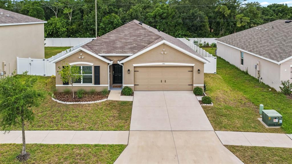 A tan, single-story house with a two-car garage and a white vinyl fence — 1911 BLUE STREAM STREET, RUSKIN, FL